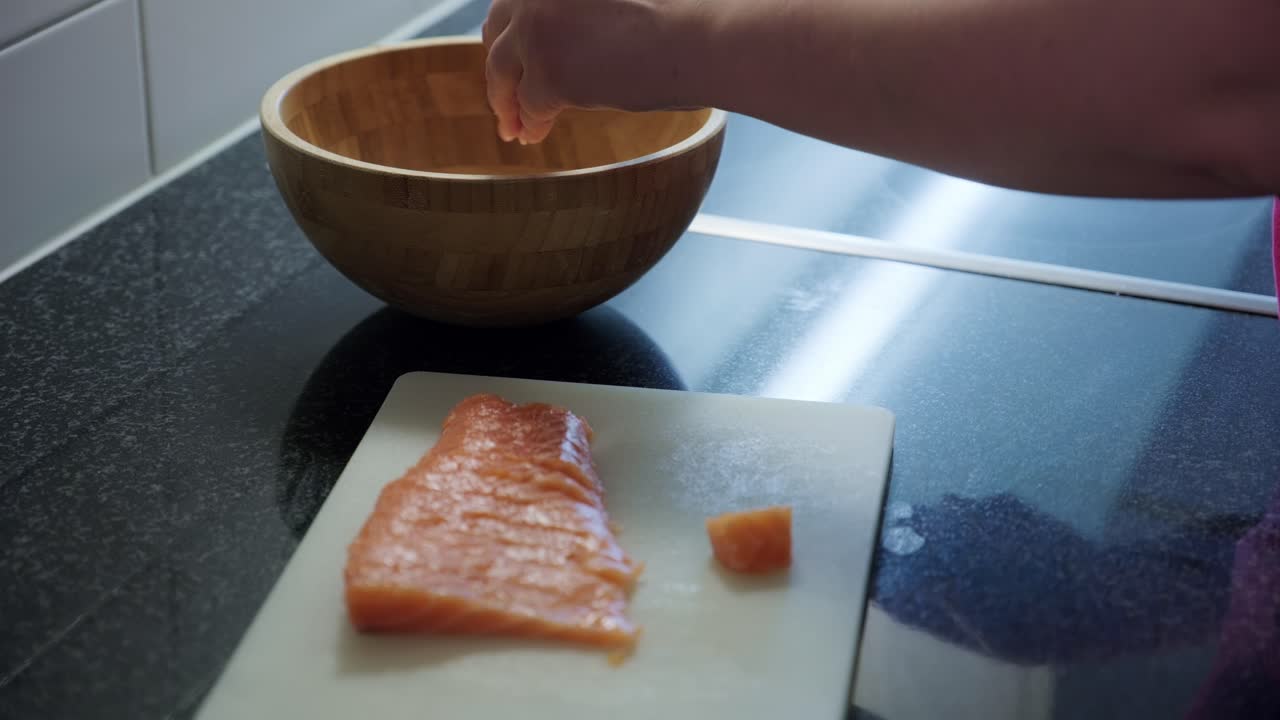 Static shot of woman hands putting raw salmon in a wooden bowl, interior