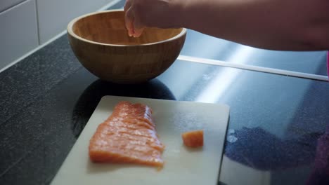 Static shot of woman hands putting raw salmon in a wooden bowl, interior