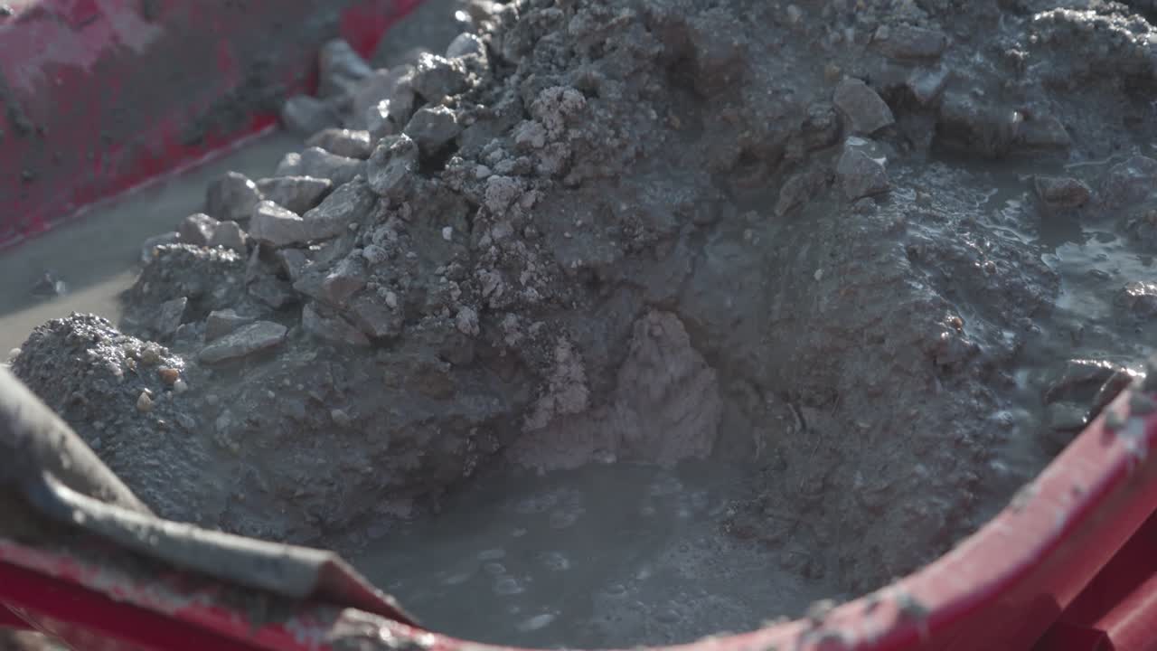 Obrero de construcción mezclando cemento en una carretilla. Primer plano