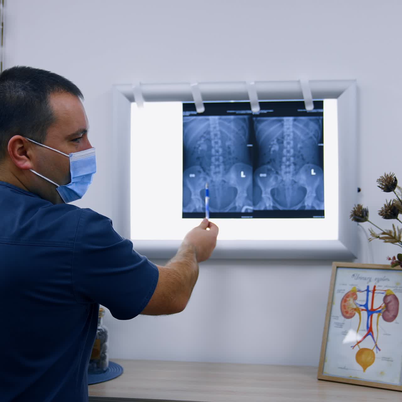 Mid-aged male medic wearing mask talks to patient pointing at x-ray scan. Health check up in modern hospital