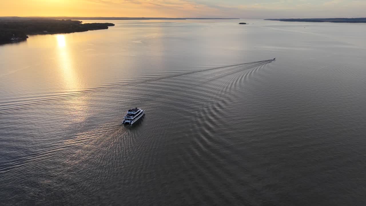 Foto aerea di un catamarano che naviga in acque calme con riflessi del tramonto e l'atmosfera estiva di un'isola solitaria