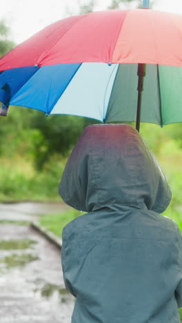 kid wanders in rainy park with parasol. small child explores spring garden injecting splash of brightness by colorful umbrella in damp atmosphere