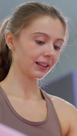 el instructor de marrón observa de cerca y guía a la mujer de rosa realizando abdominales, el brazo de la mujer se mueve en movimiento mientras una luz brillante brilla por detrás, reflejándose alrededor de la cabeza del instructor en un estudio de fitness