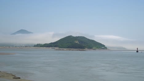 montañas de la isla de ganghwado cubiertas de densas nubes de niebla rodeadas de agua de mar amarilla en corea del sur, boya de navegación roja flotante, marea baja, marea baja