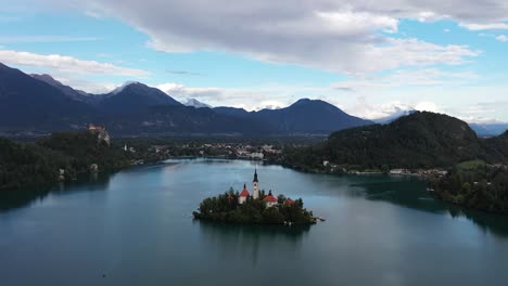 a drone orbits the fairytale island of lake bled, circling the church at its heart while alpine mountains rise majestically beyond, shimmering water and lush greenery completing slovenia’s