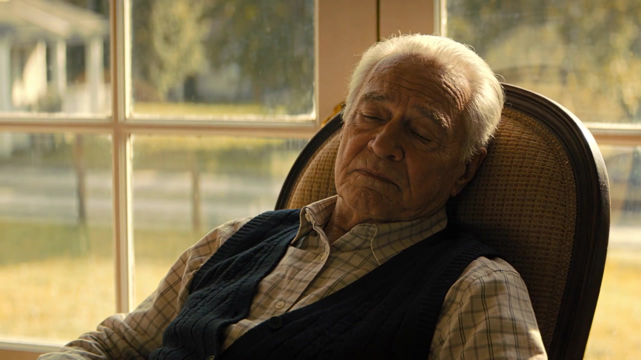 Leaning back senior man napping in chair at home by multi-pane window, wearing knitted vest