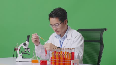 side view of asian man scientist sitting and making experiment with test tube on the table with microscope in the green screen background laboratory