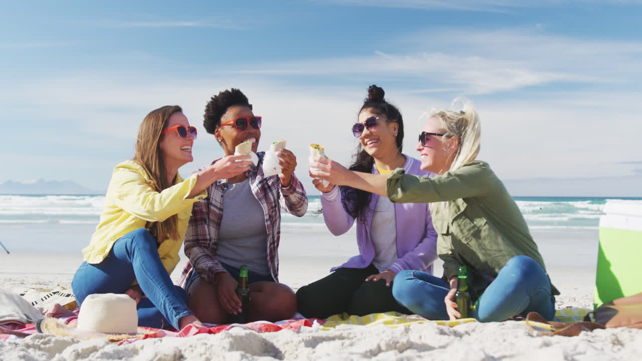 Gruppo felice di diverse amiche che si divertono, facendo un picnic in spiaggia