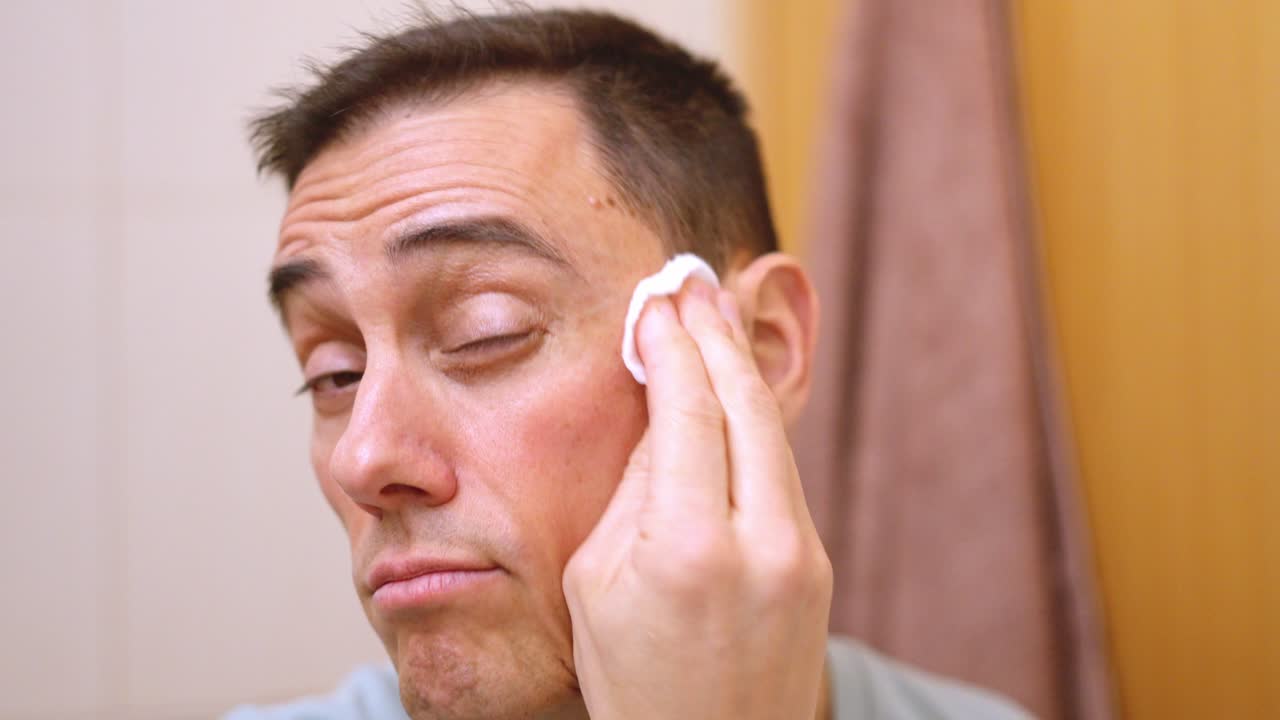 Adult man using cotton pad for facial cleansing