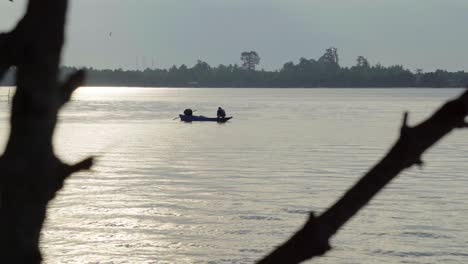 An-abstract-silhouette-shot-of-a-Local-Thai-fisherman-crouched-over-the-bow-of-his-boat-preparing-a-fishing-net-on-a-beautiful-morning-on-Chanthaburi-River,-Thailand