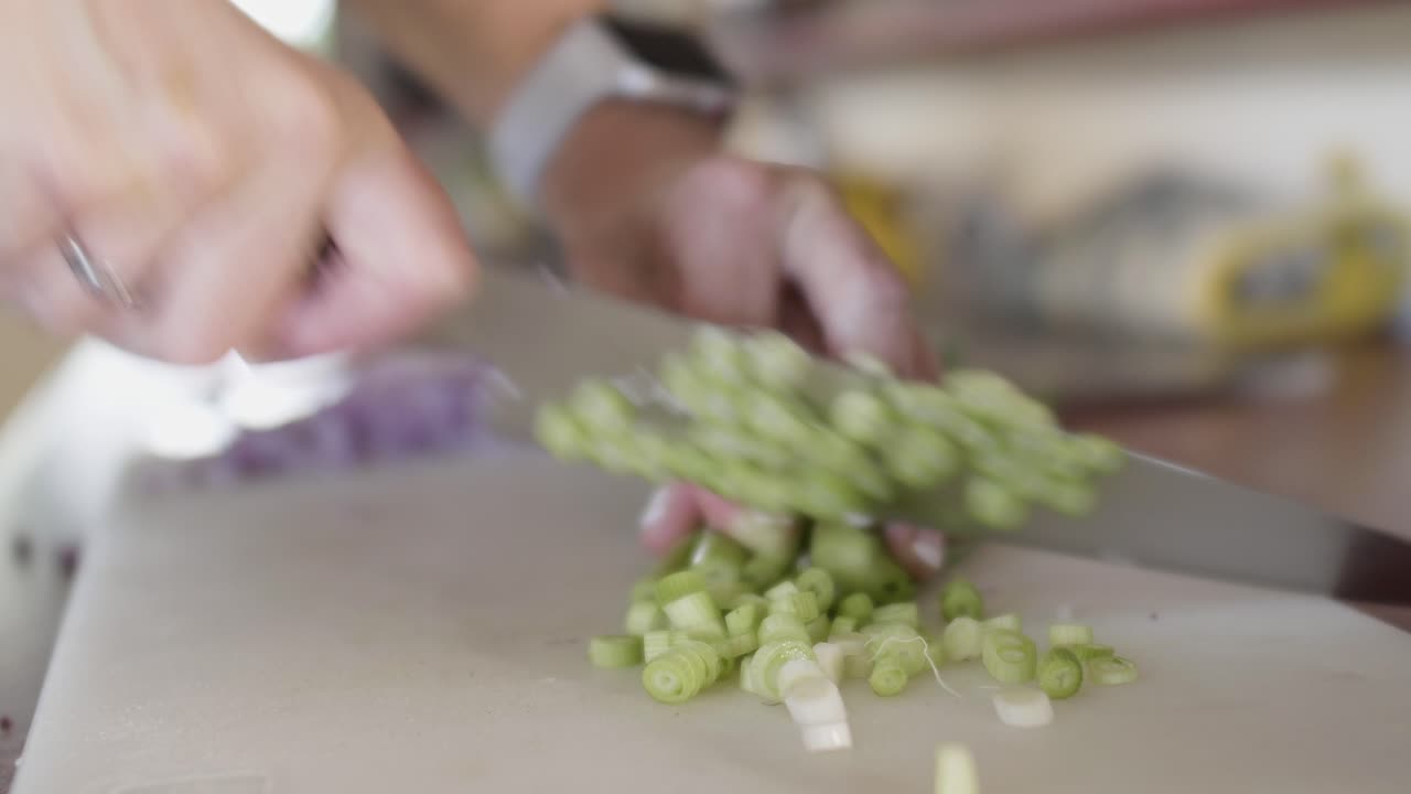 A chef slicing green spring onion on a conf board