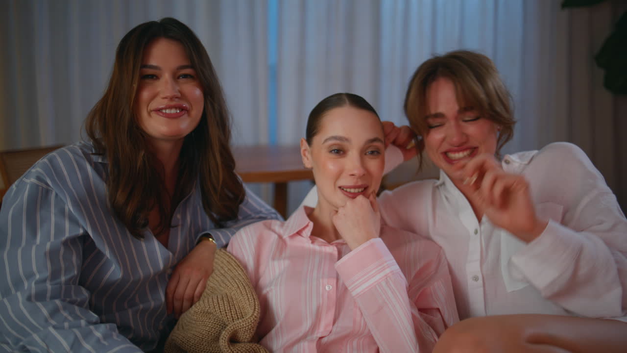 Pajamas women laughing movie sitting night home couch closeup. Smiling friends
