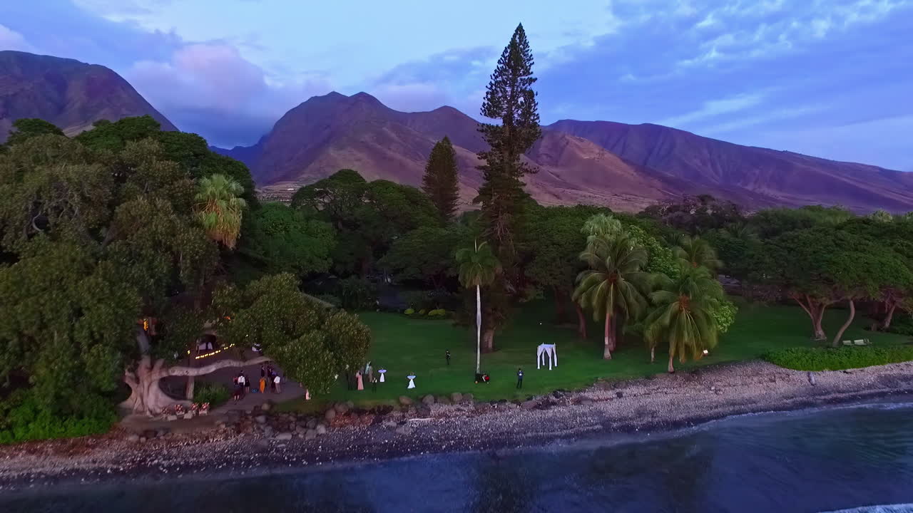 dron aéreo que se mueve hacia adelante sobre la función que va en el resort junto a la playa en olowalu, hawaii con la vista de la cordillera en el fondo