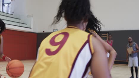 diverse female basketball team training with male coach in indoor court, in slow motion