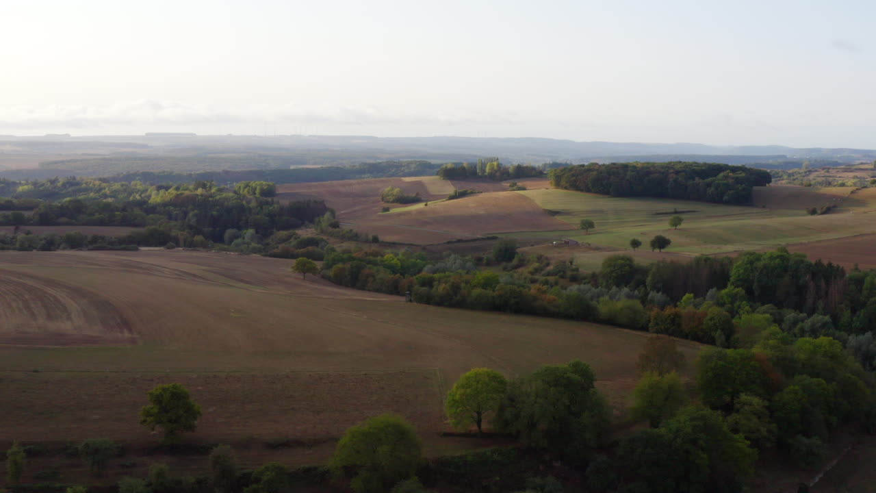 High Quality aerial view of rolling Luxembourg farmland with soft morning light, gentle hills, scattered trees and quiet country roads, warm tones, calm atmosphere, cinematic clarity