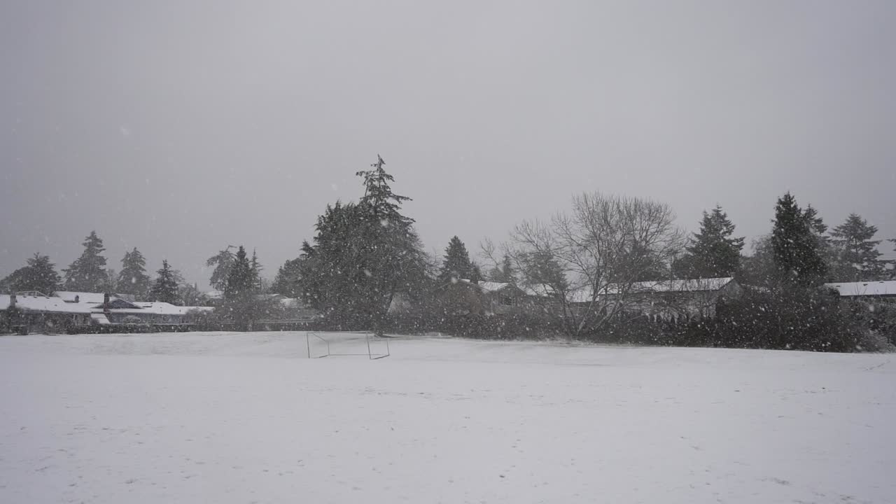 imágenes en cámara lenta de una ligera nevada con vistas a un campo de fútbol cubierto de nieve en un barrio residencial