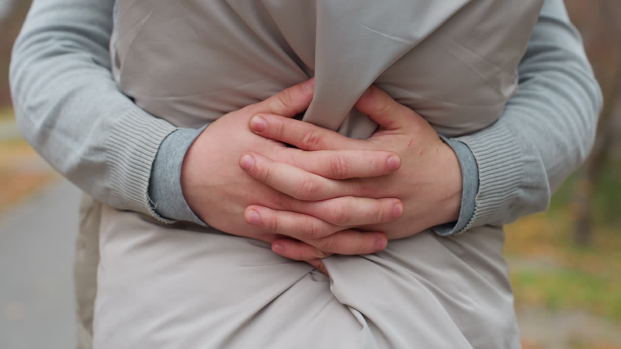 Close up of person holding another closely around waist in affectionate embrace, hands gently gripping light jacket, showing warmth, intimacy, and connection in outdoor setting