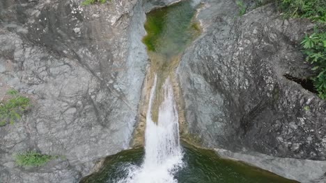 aerial tilt down shot of las yayitas waterfall with flowing water into lake in bani, dominican republic