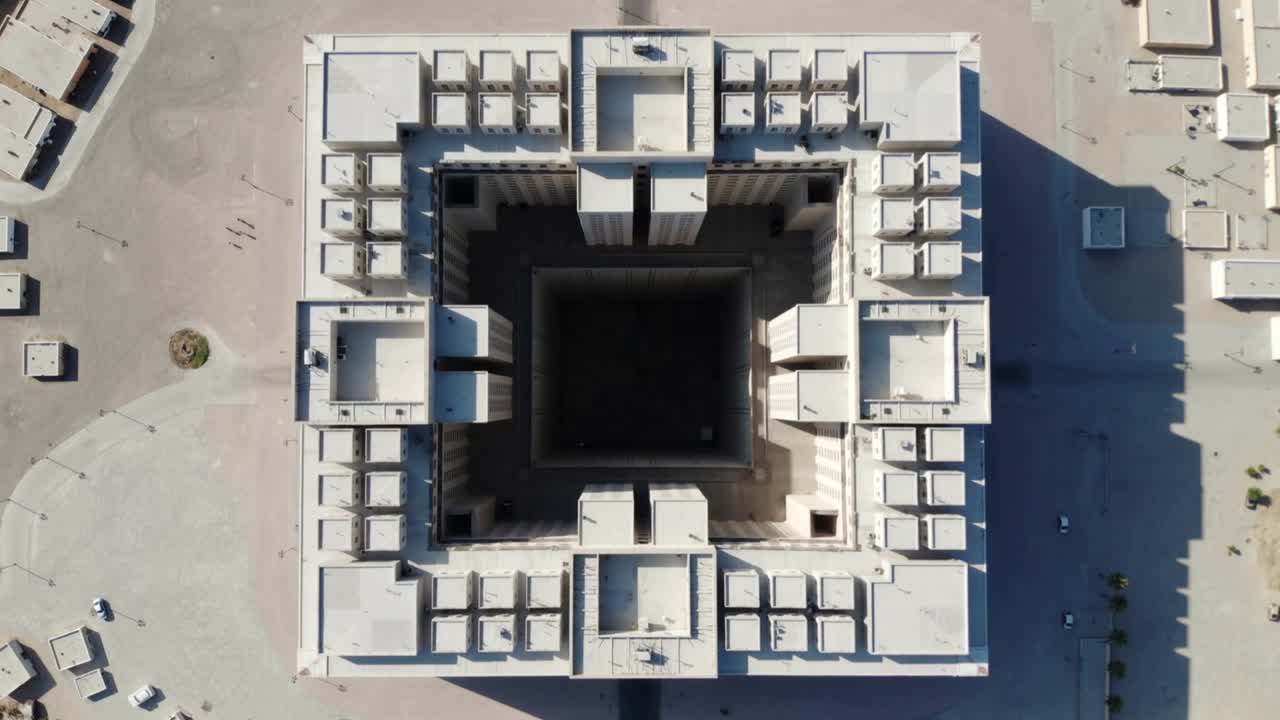 Un drone che si avvicina rivela il tetto di un grande edificio quadrato in una piazza per catturare l'atrio e le unità sul tetto.