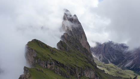 Drone-flight-over-Seceda-ridge-with-view-of-Fermeda-Towers-in-clouds,-Dolomites