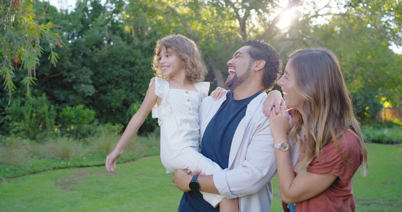 Família diversa: pai segurando a filha que aponta para a esquerda, enquanto os pais se viram para observar o jardim, com a filha de vestido branco.