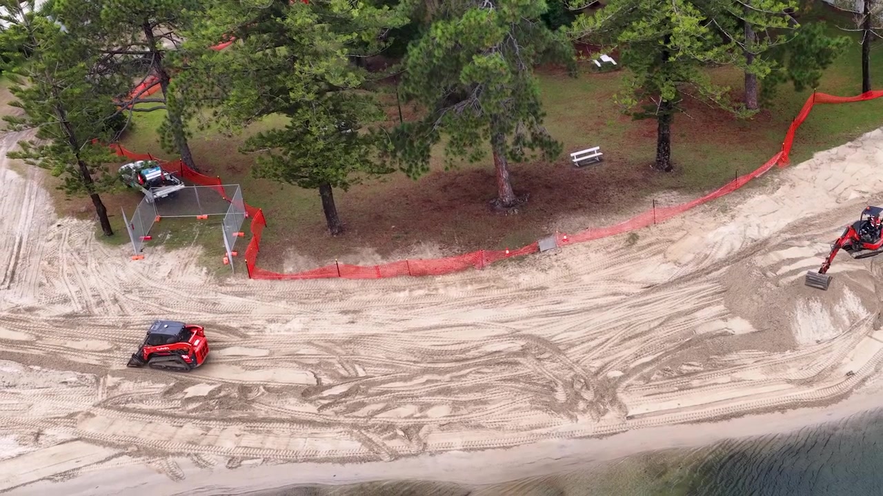 Ripresa aerea con drone dall'alto di macchinari pesanti che spostano sabbia durante un progetto di ripristino della spiaggia costiera