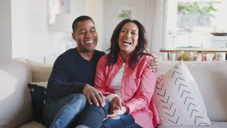 middle aged african american couple embracing on the sofa in their living room laughing, close up