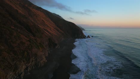 northern california waves crashing bluffs cliffside mountain rocky rugged remote coastline aerial drone usal beach campground sunset sinkyone wilderness sur swell black sand rocky shore forward motion