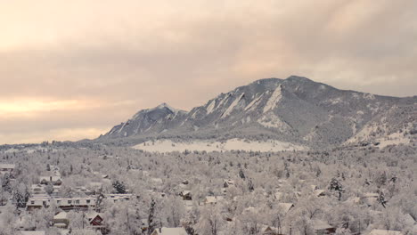 high drone shot moving right of boulder colorado and rocky flatiron mountains after large winter snow storm covers trees, homes, streets, and neighborhood in fresh white snow