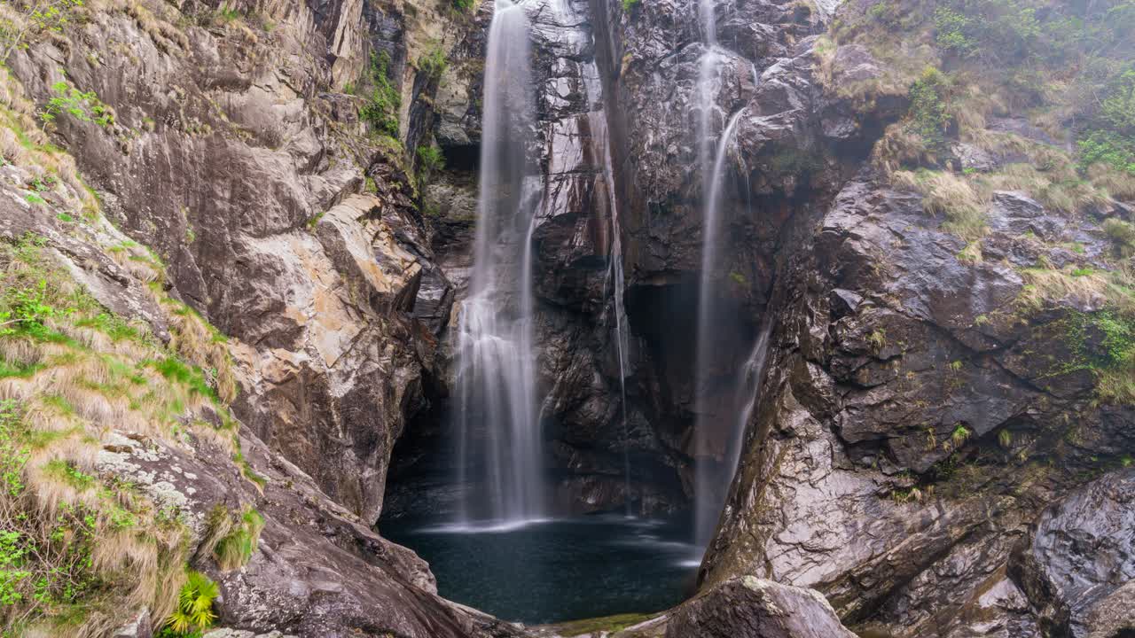 This still timelapse captures a cascading waterfall (long exposure) in Locarno, Switzerland. Water flows over rugged rock formations, forming silky streams against moss-covered cliffs.