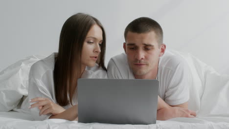 una pareja viendo una computadora portátil en la cama.