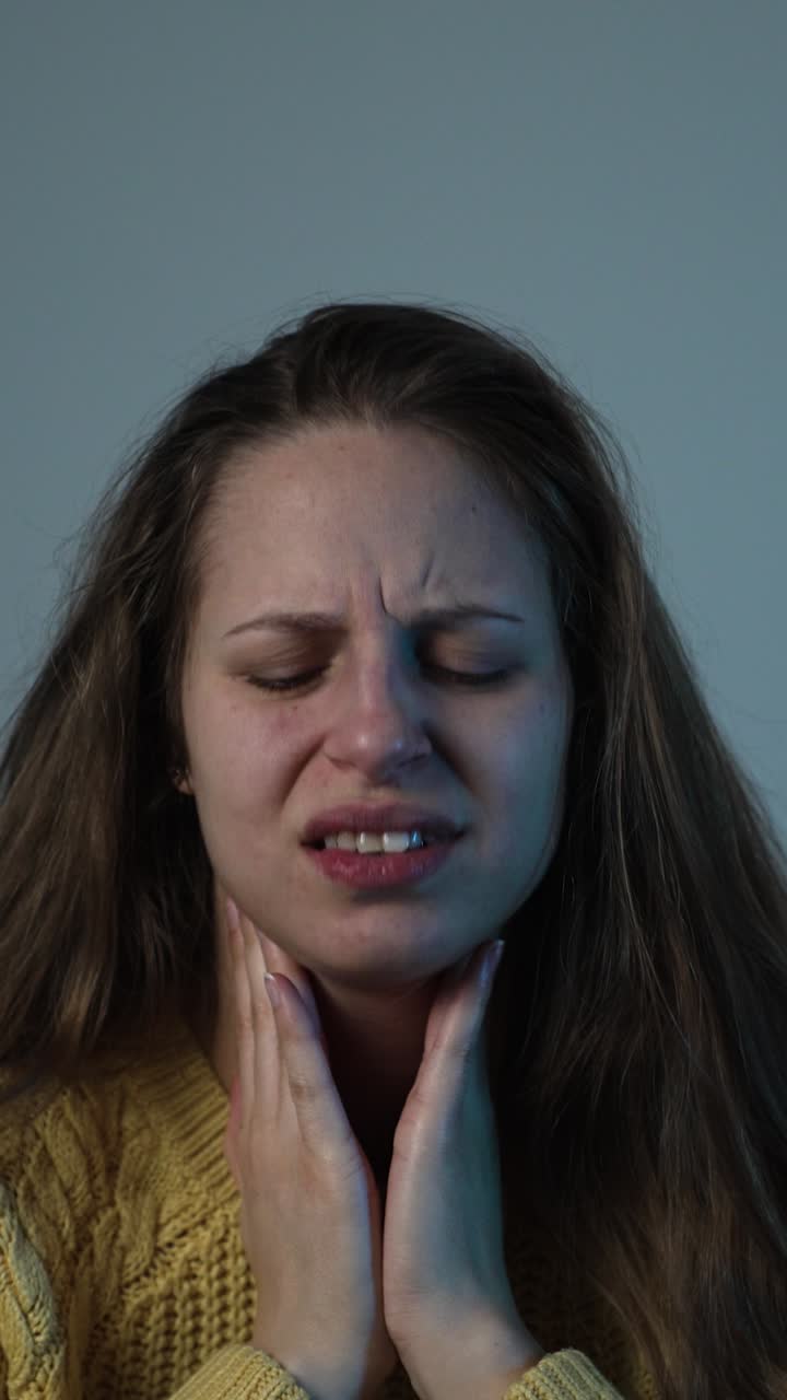 Una donna con l'influenza stagionale si tiene la gola e fa un'espressione dolorosa, mostrando disagio e i tipici sintomi di mal di gola a casa.