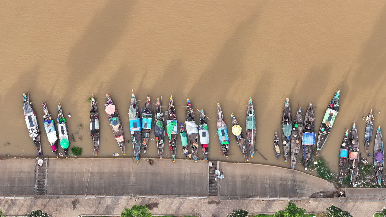 Overhead aerial video of colorful wooden boats docked along the muddy banks of the Mekong River in Phnom Penh
