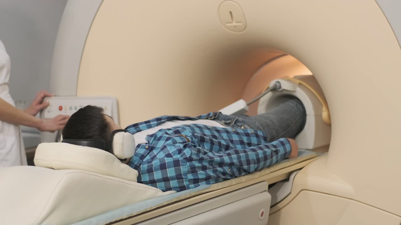 mujer médico hace escaneo de resonancia magnética de la articulación de la rodilla. joven paciente en la mesa automática entra en una máquina de resonancia eléctrica de tipo cerrado usando auriculares de aislamiento de ruido. equipo moderno, bobina en la rodilla del paciente