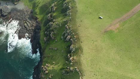 aérea de arriba hacia abajo, unidades 4x4 cerca del borde de los acantilados oceánicos, playa rocosa