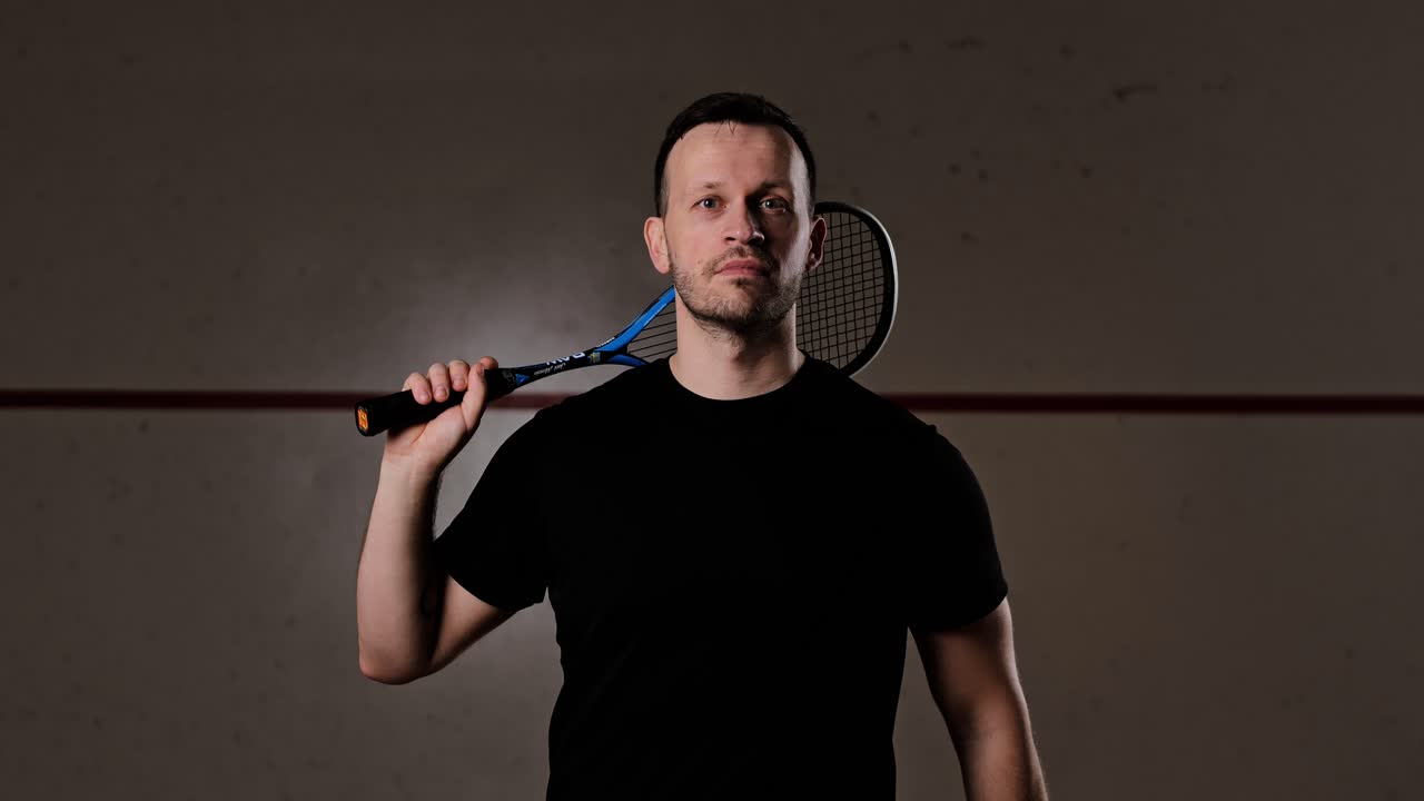 Athlete confidently looks at camera, tosses squash ball in dramatic slow motion