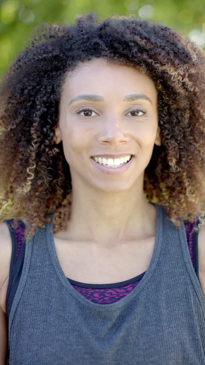 Vertical video portrait of biracial woman with long curly hair smiling in sunny garden, slow motion