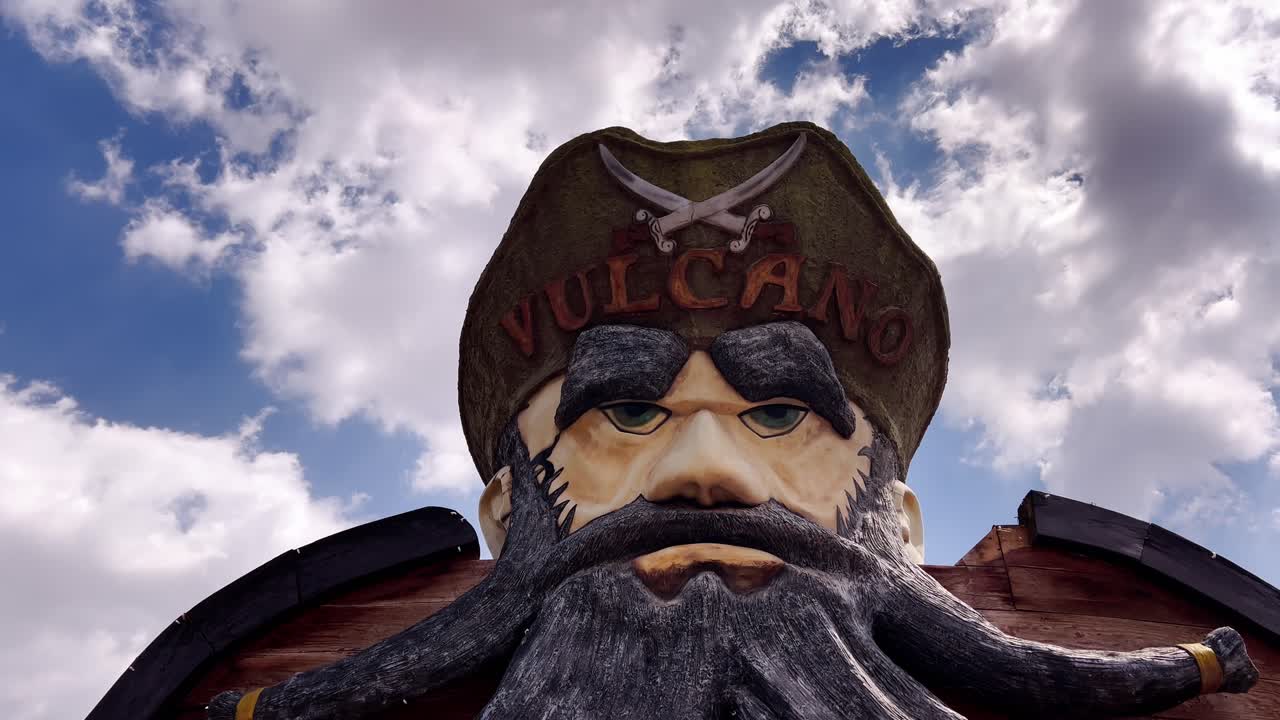 A dramatic tilt-down shot of a large pirate face sculpture set against a cloudy sky at Volcanic park in Orizaba, Puebla, Mexico.