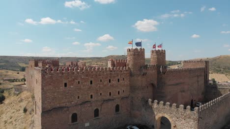 Vista-De-Drones-Del-Castillo-De-Siguenza,-Actualmente-Parador-De-Turismo,-Y-Sus-Banderas-Españolas-Y-Europeas-Ondeando