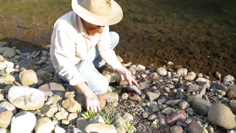 a bushman prepares a brown trout by the side of a river in the australian high country