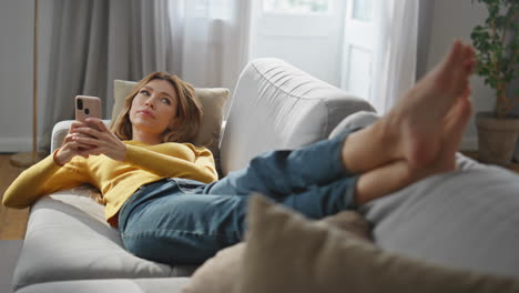 dreamy girl relaxing mobile phone at comfortable sofa. woman answering message