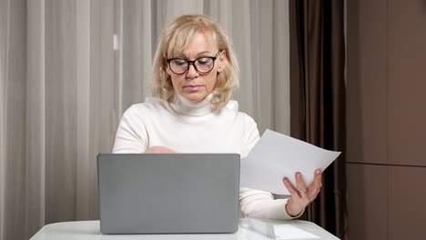 mujer de mediana edad con gafas cuenta las facturas de servicios públicos en la mesa