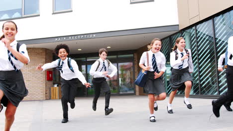 group of high school students wearing uniform running out of school buildings towards camera at the end of class