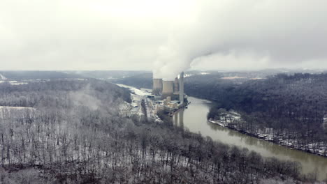 Drone-shot-towards-a-power-station-on-a-river-surround-by-snow-covered-woods