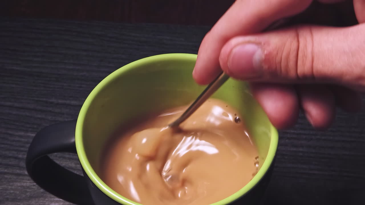 Close-up slow motion of mixing black coffee with milk by a man on wooden table in the kitchen