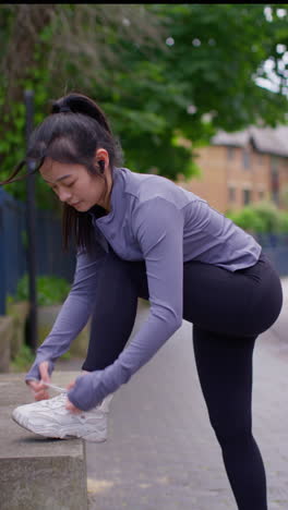 Vertical-Video-Of-Young-Woman-Tying-Laces-On-Training-Shoe-And-Stretching-Before-Exercising-Running-Along-Urban-Street-1