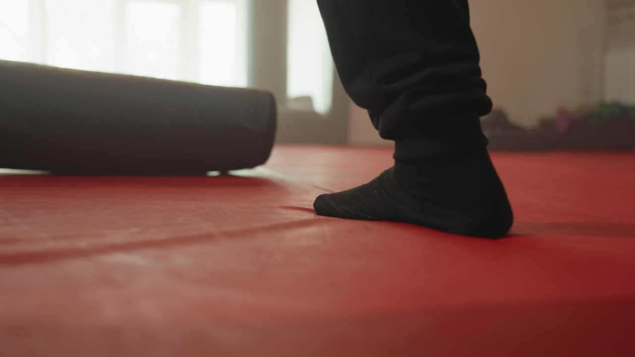Boxer foot in black sock firmly planted on red mat during training session in gym, emphasizing stance, grounding, stability, balance, and preparation for combat practice with dummy equipment in background