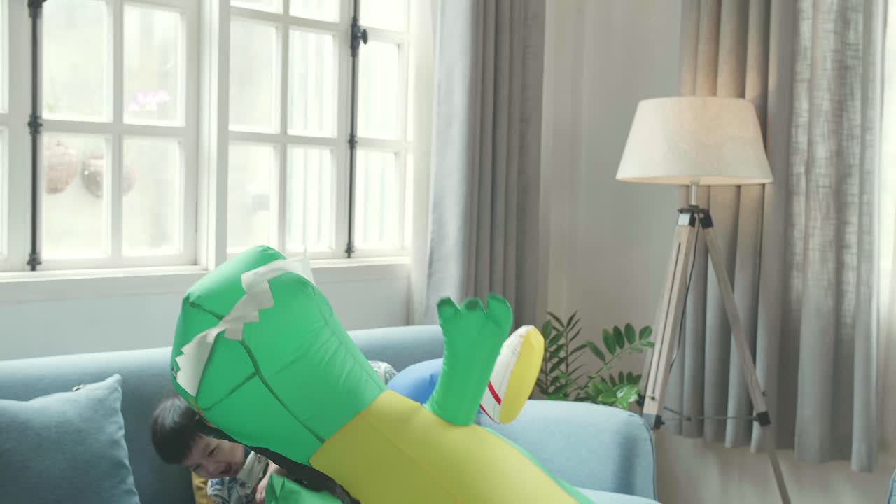 Tried Asian Father Carrying His Son While Ride Dinosaur Toy In Modern House Living Room