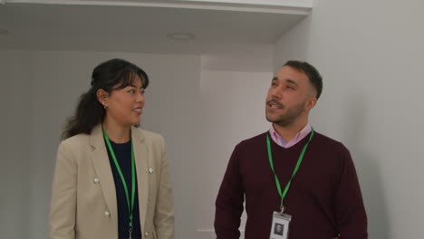 Male-And-Female-Teachers-Wearing-Security-Lanyards-Talking-As-They-Walk-Along-Corridor-In-School-Building-Together-1