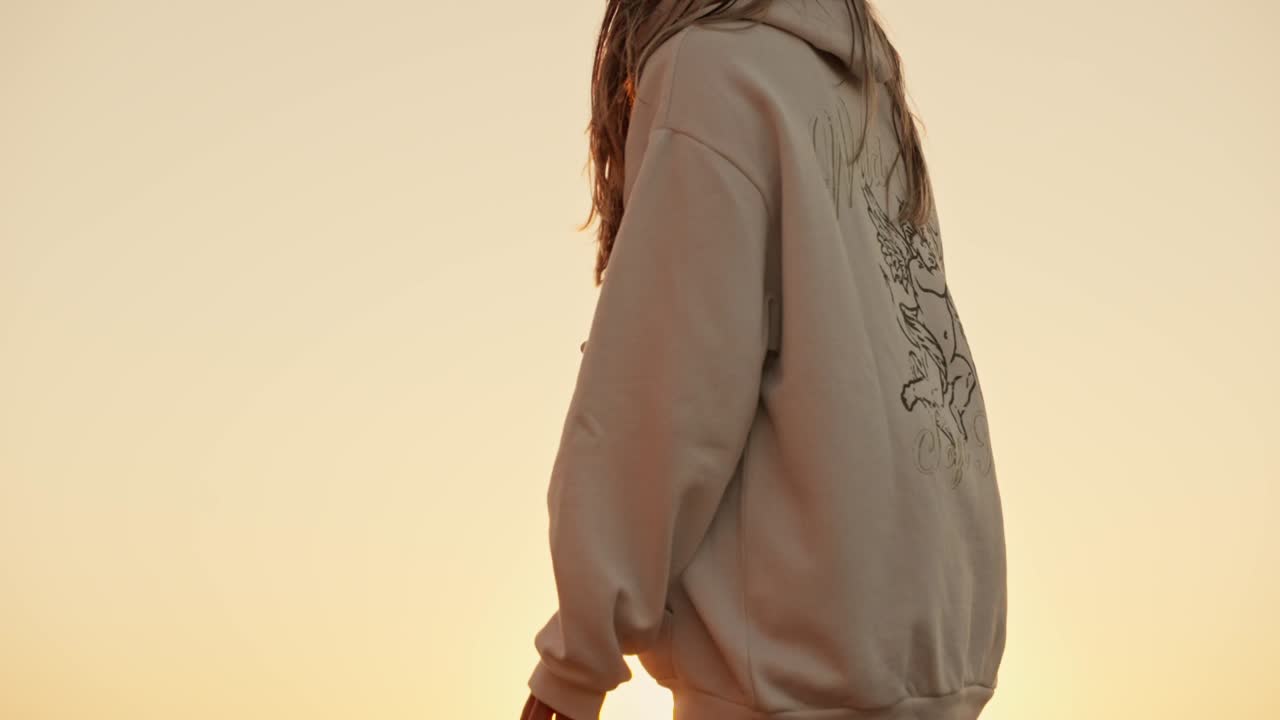 adolescente en pantalones cortos y sudadera mirando el sol poniéndose sobre el mar desde las rocas
